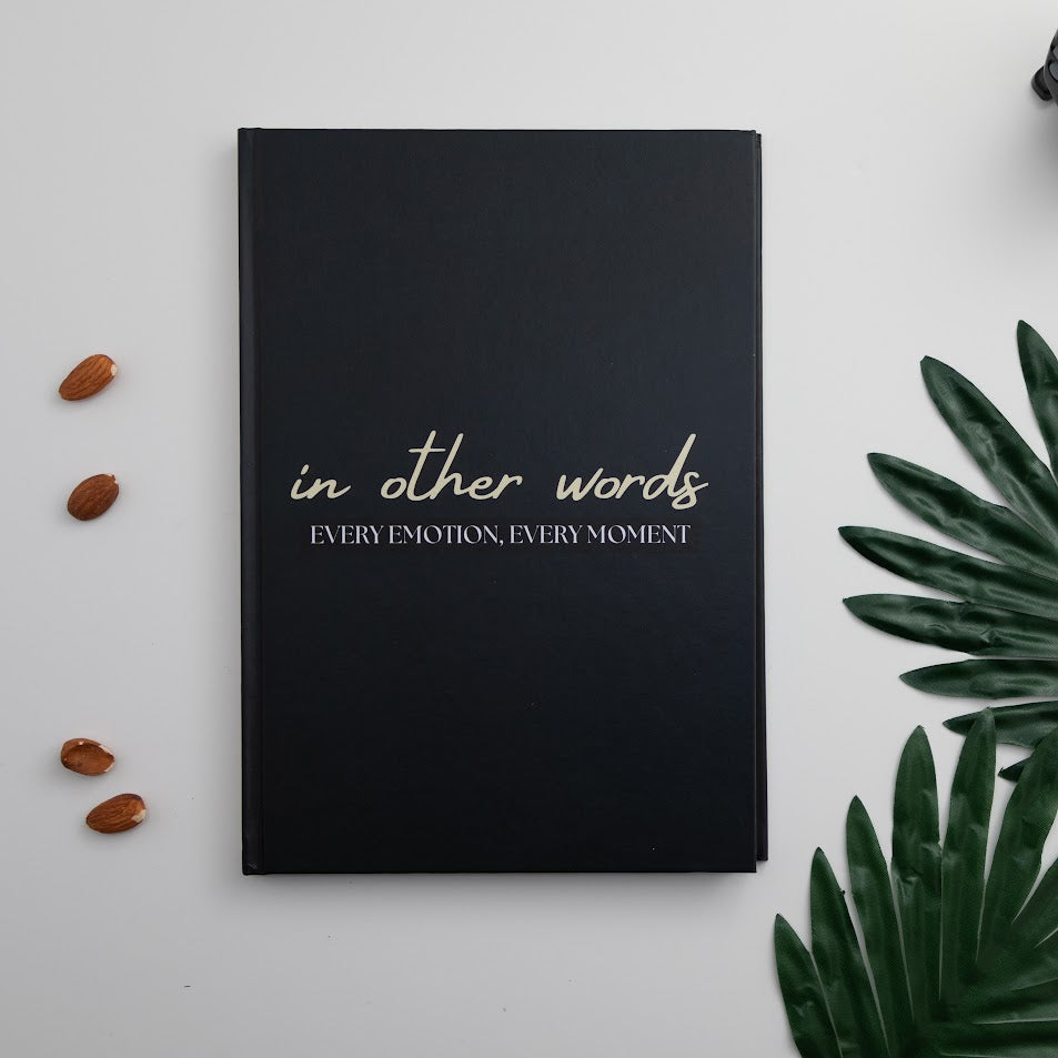 The book in other words next to some green leaves on a counter